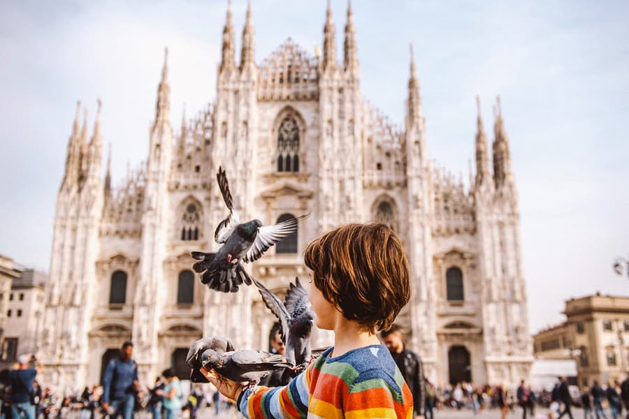 Pojke som matar duvor framför domkyrkan i Milano